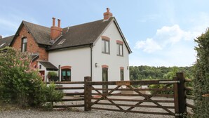 A two-story house with a white facade and a brick section, a gravel driveway, and a wooden gate. - Minton Lane Cottage (Church Stretton)