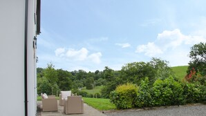 A patio with outdoor furniture, a gravel path, and a view of a green landscape with trees and hills. - Minton Lane Cottage (Church Stretton)