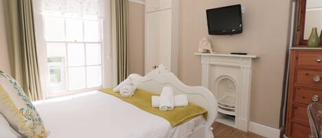 A hotel room with a bed, a television mounted on the wall, a fireplace, and a wooden dresser.