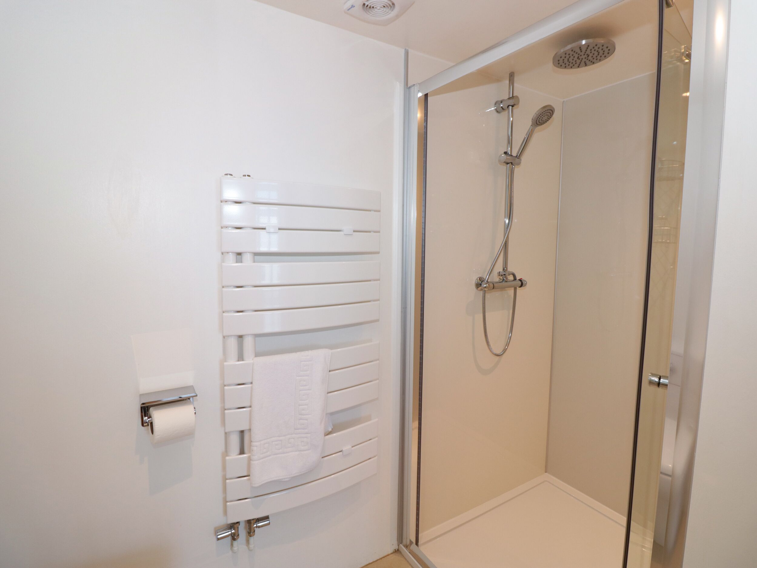 A modern bathroom with a glass shower enclosure, a towel rack, and a toilet paper holder.