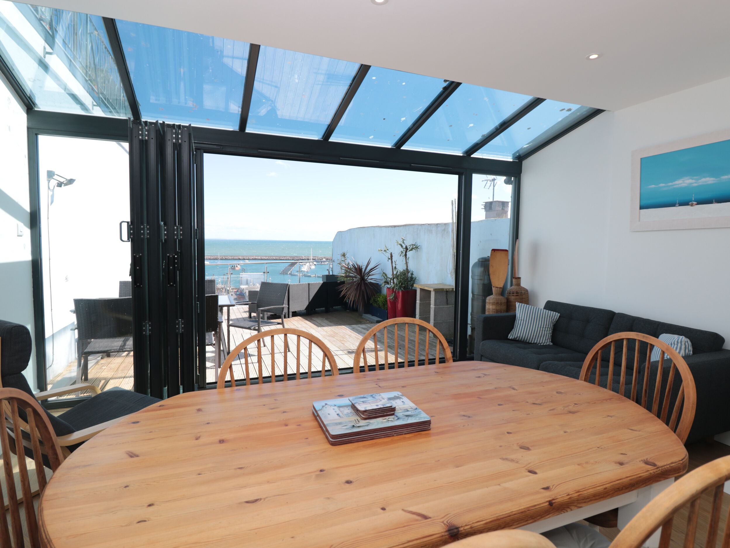 Ein moderner Essbereich mit Holztisch und -stühlen, einer Couch und Meerblick durch große Glasüren.