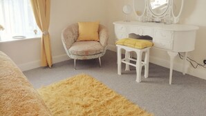 Un dormitorio con tocador, una silla, un felpudo mullido y una ventana con cortinas.