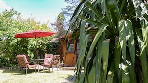 A patio with a red umbrella, two wicker chairs, and a small table. - Garden View (Newquay)