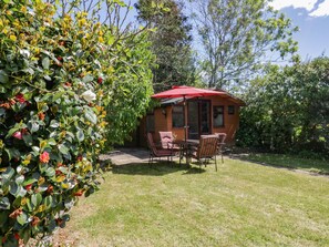 A wooden cabin with a red umbrella, a patio table, and chairs.