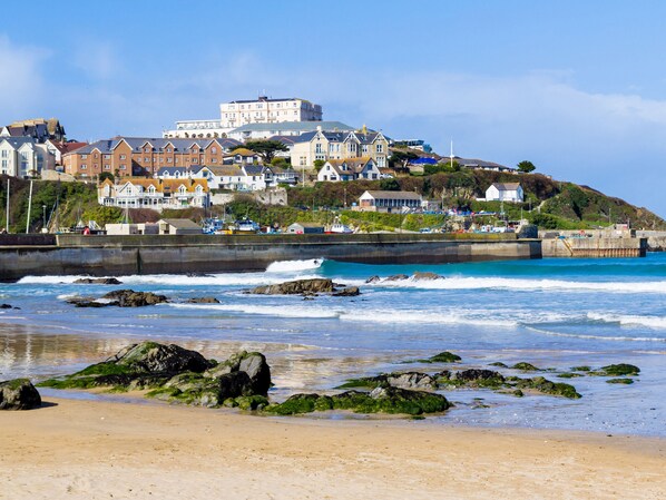 A coastal town with a prominent hilltop building, a sandy beach with rocks, and a clear blue sea.