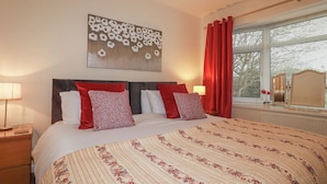 A neatly made bed with floral bedding, a headboard, and red and white pillows. - Garden View (Newquay)
