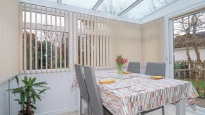 A conservatory with a table set for dining, chairs, a potted plant, and a vase with flowers. - Garden View (Newquay)
