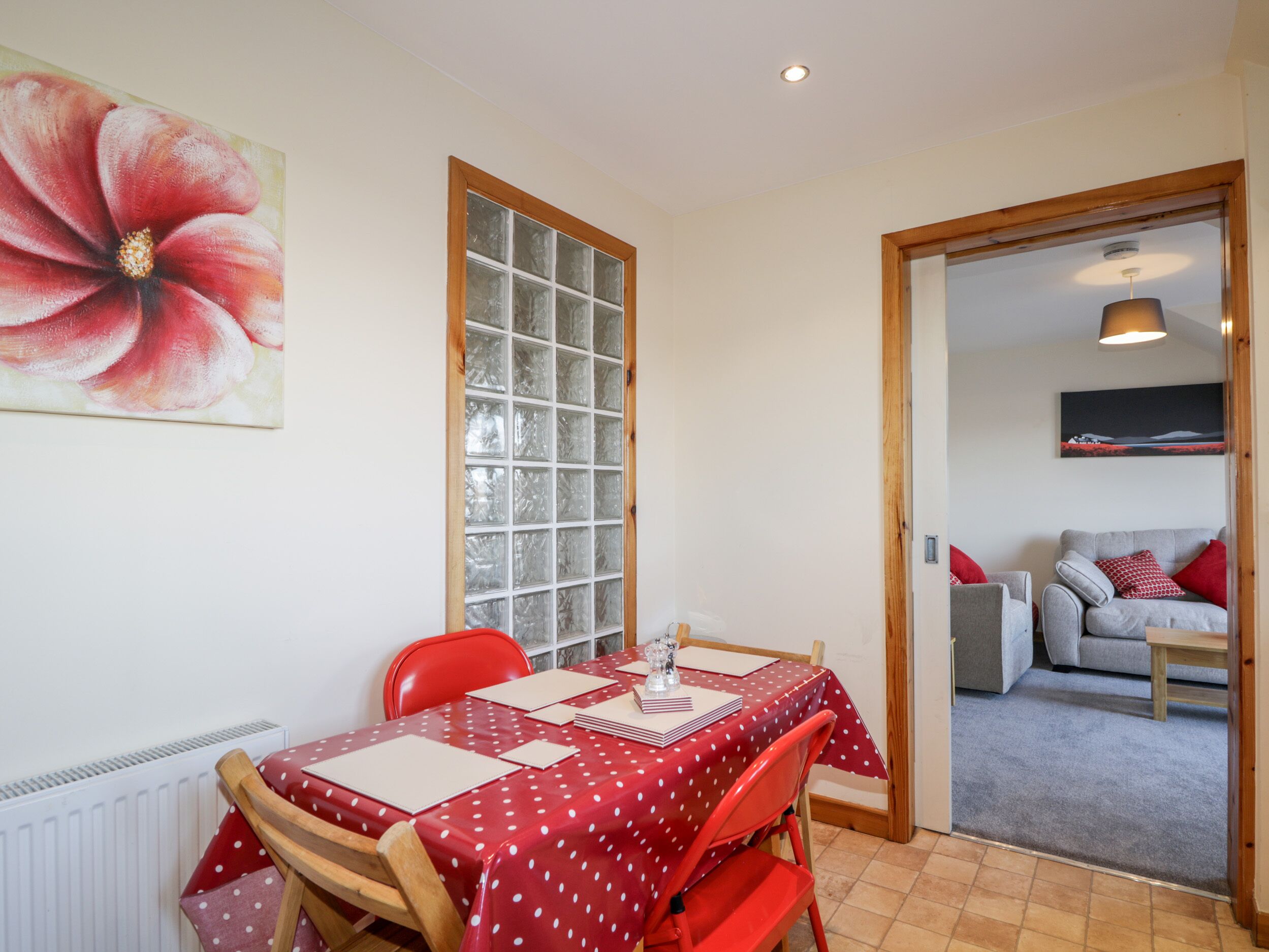A dining area with a table set for four, a red polka dot tablecloth, and a large window with frosted glass panes.