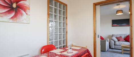 A dining area with a table set for four, a red polka dot tablecloth, and a large window with frosted glass panes.