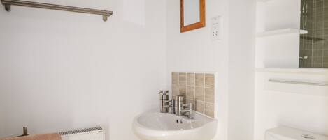 Un baño con lavamanos blanco, toallero, espejo y radiador.