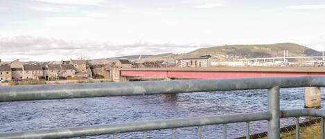Ein Fluss mit einem Metallgeländer im Vordergrund, eine rote Brücke im Hintergrund und Gebäude am gegenüberliegenden Ufer.