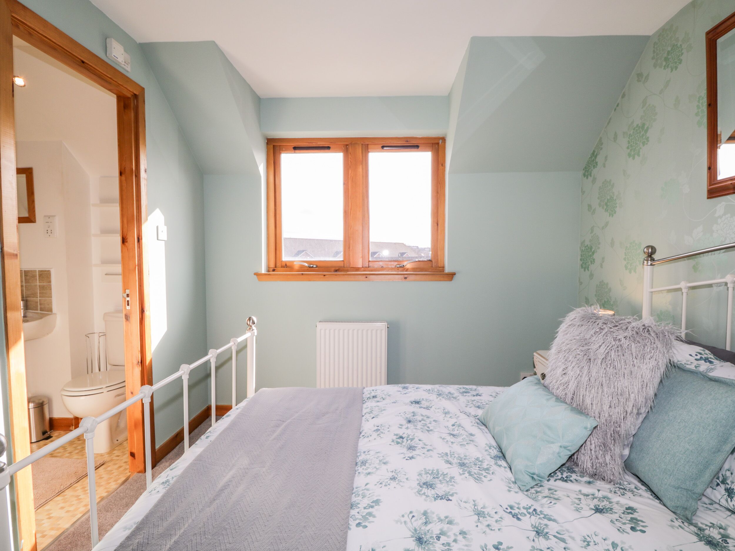 A bedroom with a bed, a window, a radiator, and a door leading to a bathroom.