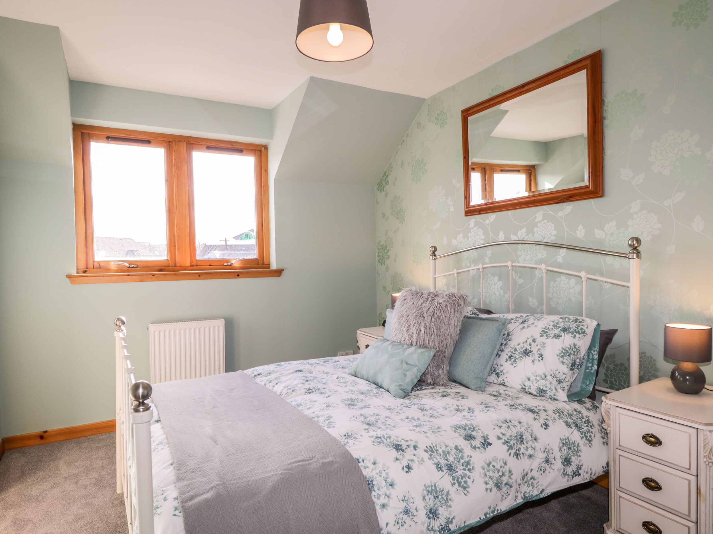 A bedroom with a bed, bedside table, lamp, and a window.