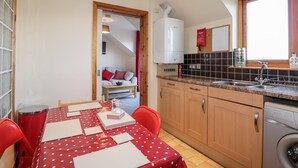 Una cucina compatta con zona pranzo, caratterizzata da una tovaglia rossa e bianca a pois, mobili in legno, lavastoviglie integrata e una finestra con vista.