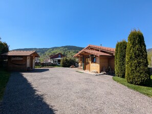 A wooden lodge with a gravel driveway, a mountain backdrop, and a clear sky.