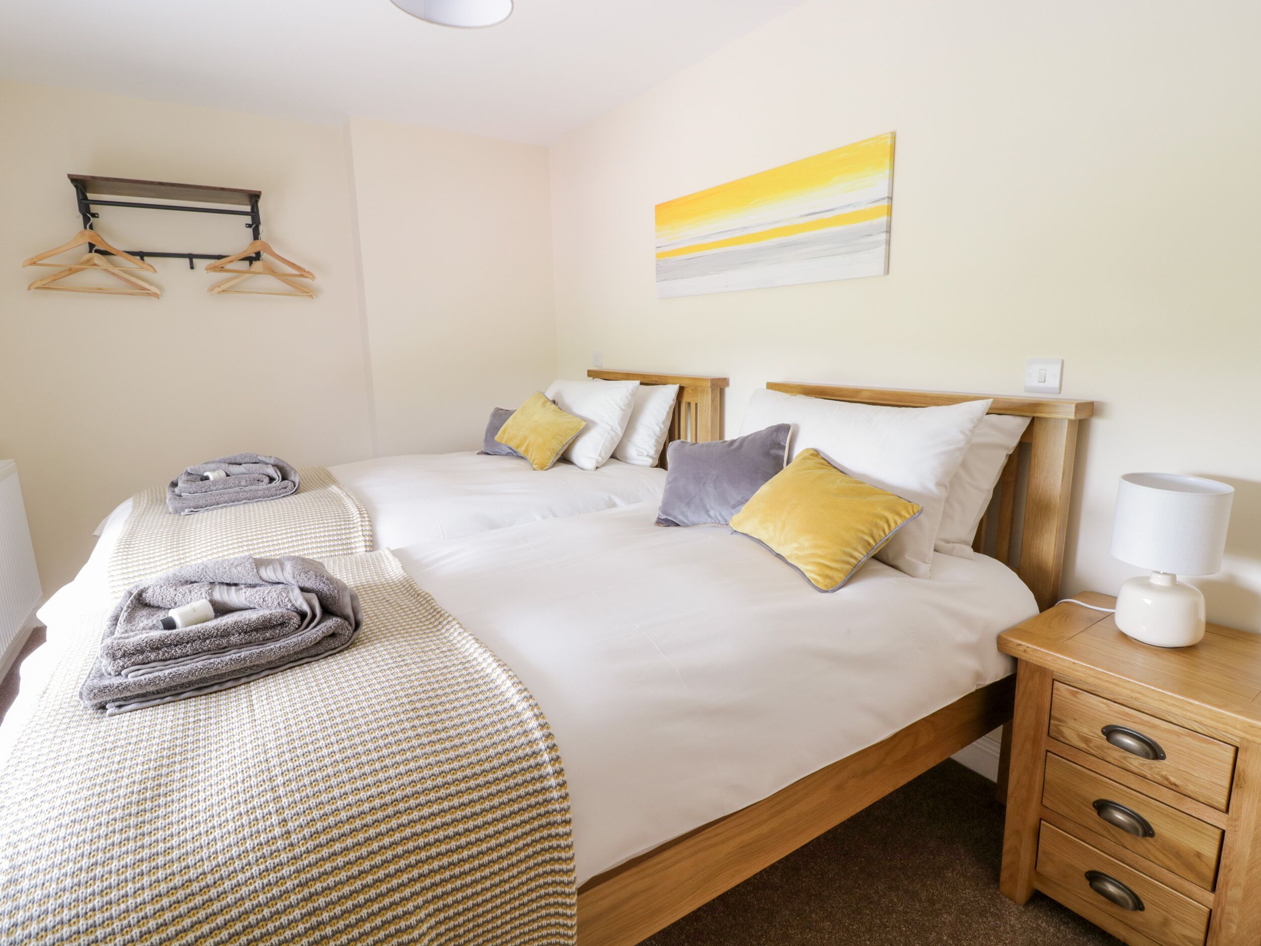 A neatly made double bed with a wooden headboard, two bedside tables, a lamp, and a wall-mounted towel rack.