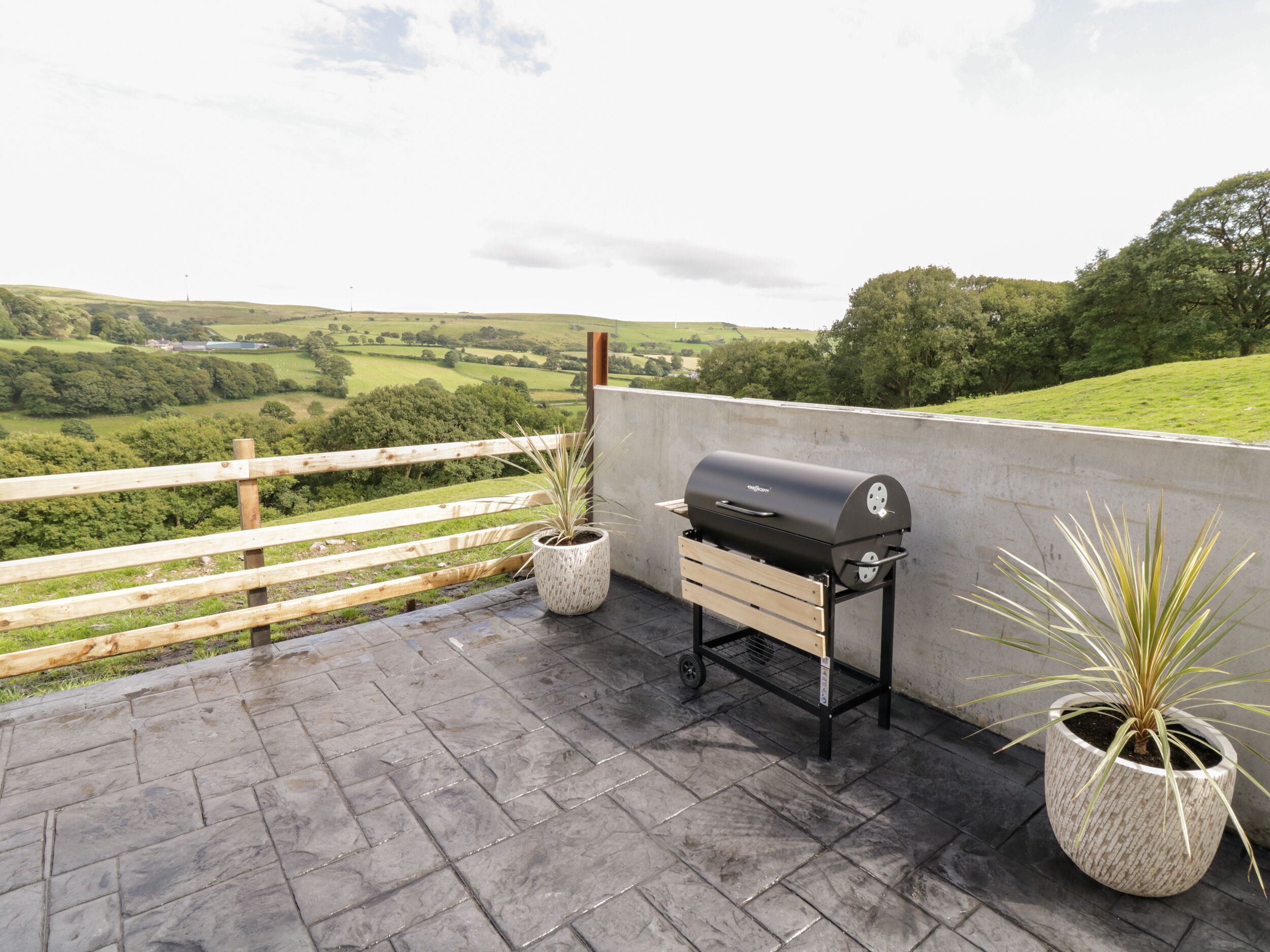 Un barbecue installé sur une terrasse en toit-terrasse, offrant une vue sur des champs verdoyants et des collines.