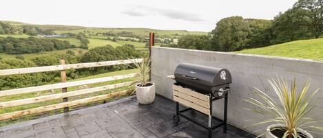 Un barbecue installé sur une terrasse en toit-terrasse, offrant une vue sur des champs verdoyants et des collines.
