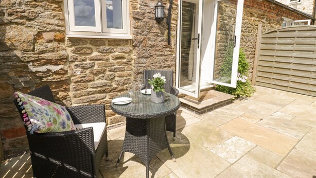 Une maison en pierre dotée d’un patio aménagé avec des meubles en osier et une table en verre.