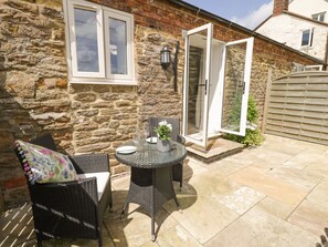 Una casa de piedra con un patio que incluye mobiliario de mimbre y una mesa de vidrio.