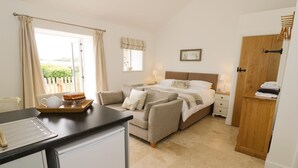 Une chambre à coucher comprenant un lit, des tables de chevet, une commode, une fenêtre avec des rideaux et une vue sur la verdure à l’extérieur.