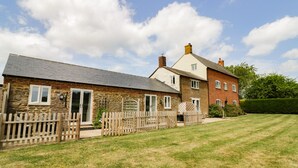 A two-story house with a stone facade and a red brick section, featuring a wooden fence and a well-maintained lawn.