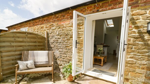A stone house with a wooden bench and a potted plant outside.