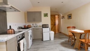 A compact kitchen with a stove, microwave, and washing machine. There is a dining area with a table and chairs. - Honeybee Cottage (Hull)