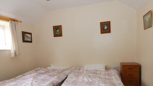 A bedroom with two single beds, a wooden nightstand with drawers, and two small framed pictures on the wall. - Honeybee Cottage (Hull)