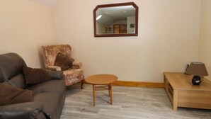 A living room with a brown leather sofa, a floral armchair, a wooden coffee table, a small wooden side table with a lamp, and a mirror on the wall. - Honeybee Cottage (Hull)