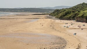 A wide sandy beach with people walking and tents set up. - Y Gogarth (Tyn-y-Gongl)
