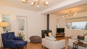 A modern living room with a sofa, a bean bag, a TV, and a fireplace. - Y Gogarth (Tyn-y-Gongl)