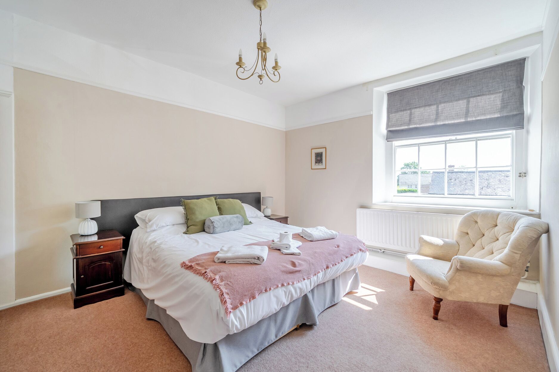 A bedroom with a bed, bedside tables, a chair, a window, and a radiator.