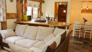 A cozy living room with a brown sofa, a dining area with white chairs, and a kitchen with wooden cabinets and a window. - Broughton Stables (Montgomery)
