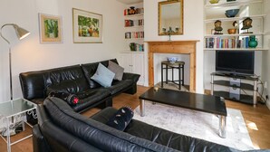 Una sala de estar con un sofá de cuero negro, una mesita de centro, una estantería, una chimenea y un televisor.
