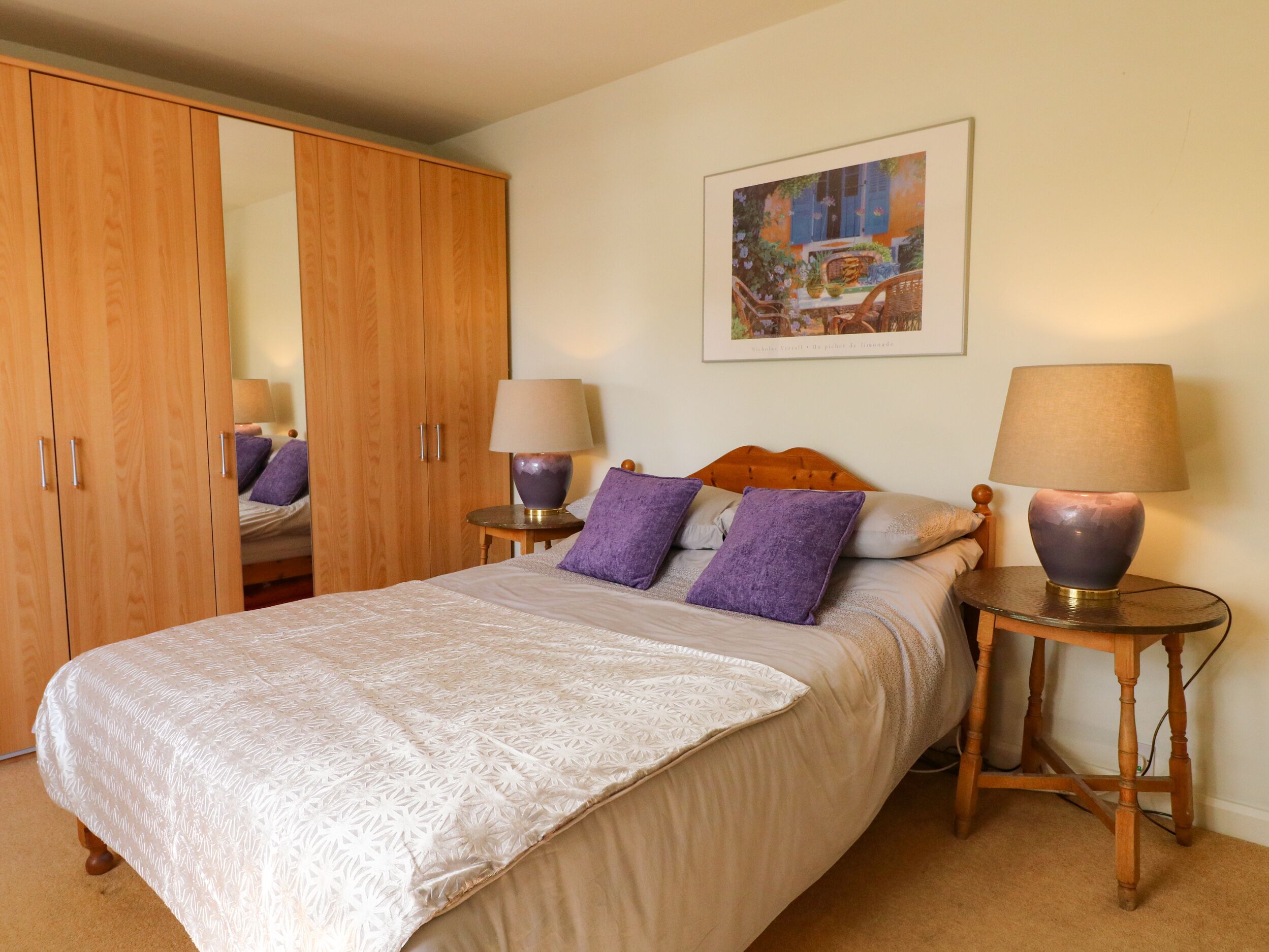 A bedroom with a bed, two bedside tables with lamps, a wardrobe, and a framed picture on the wall.
