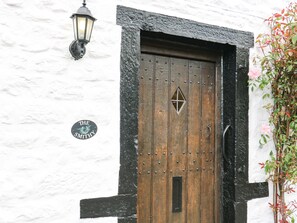 A wooden door with a diamond-shaped window, a metal handle, and a black and white textured wall. - Smithy Cottage (Skipton)
