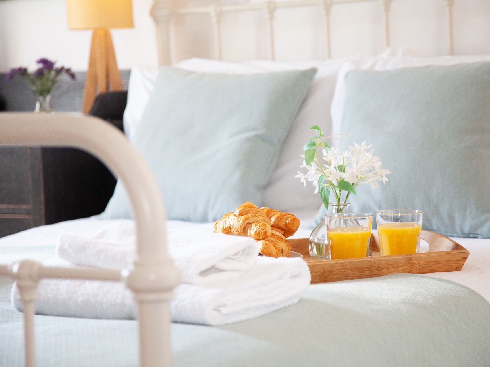 Un letto rifatto con cuscini, un vassoio con croissant, un bicchiere di succo d'arancia e un vaso con fiori.