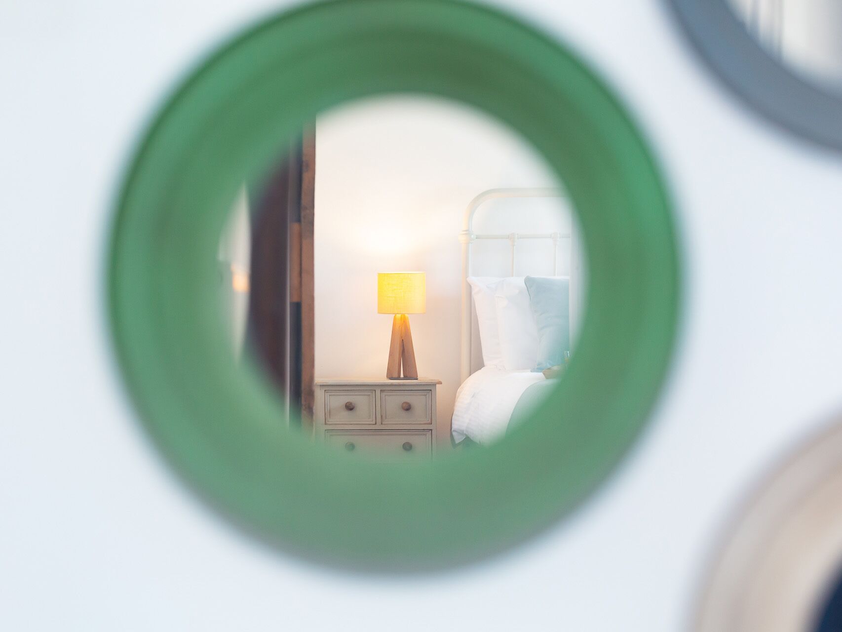 Un espejo circular que refleja una habitación con una cama, una mesita de noche y una lámpara.
