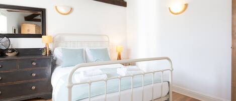 A bedroom with a white metal bed frame, a wooden dresser, a mirror, and two wall-mounted lamps.