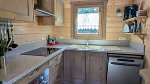 Eine kleine Küche mit Holzausstattung, einem Edelstahl-Geschirrspüler, einem Einbauofen und einem Fenster mit Blick auf Grünflächen.