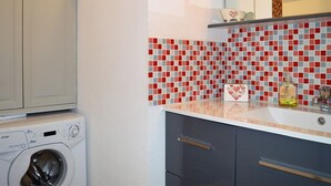 A compact kitchen with a washing machine, a tiled backsplash, and a countertop with a bottle.