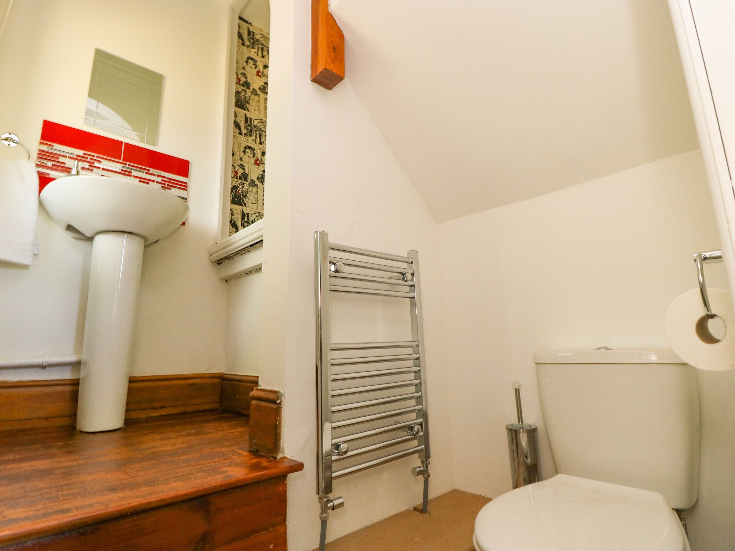 A bathroom with a white sink, a wooden bench, a towel rack, a toilet, and a radiator.
