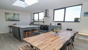 Une cuisine moderne dotée d’un îlot central, d’un coin repas avec une table et des bancs en bois, et de grandes fenêtres offrant une vue sur l’extérieur.