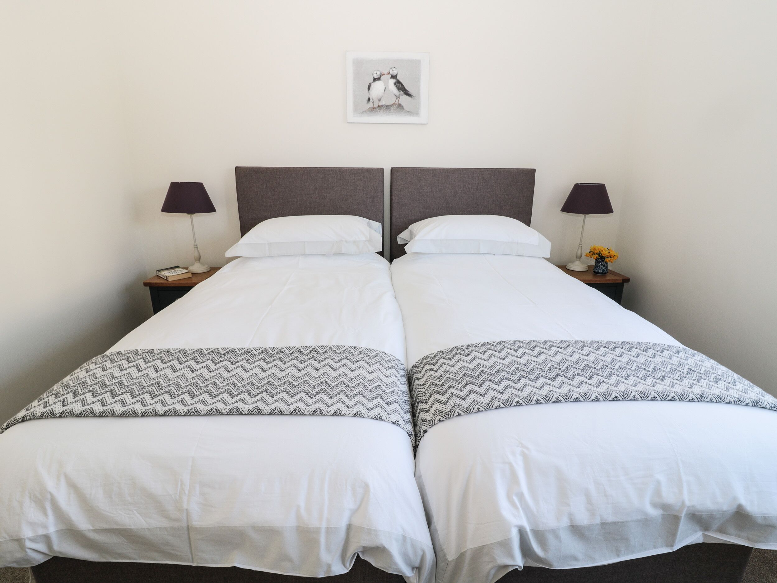 A double bed with white bedding and patterned throw pillows, two bedside tables with lamps, and a framed picture on the wall.