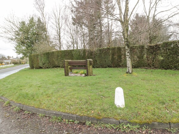 A grassy area with a wooden bench and a white headstone. - Glanton (Morpeth)