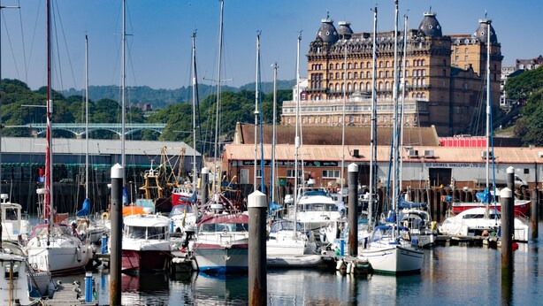 En lysthavn med flere både i havnen, en stor bygning med kuppelarkitektur i baggrunden, og en klar himmel.