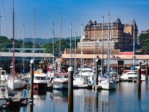 A marina with multiple boats docked, a large building with domed architecture in the background, and a clear sky. - Hook's House (Scarborough)