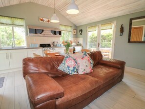 A cozy living room with a brown leather sofa, a wooden dining table, and a kitchen in the background. - The Hen House (Rugeley)