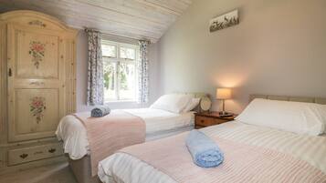 A bedroom with two beds, a wooden wardrobe, a window with floral curtains, and a wall-mounted picture.